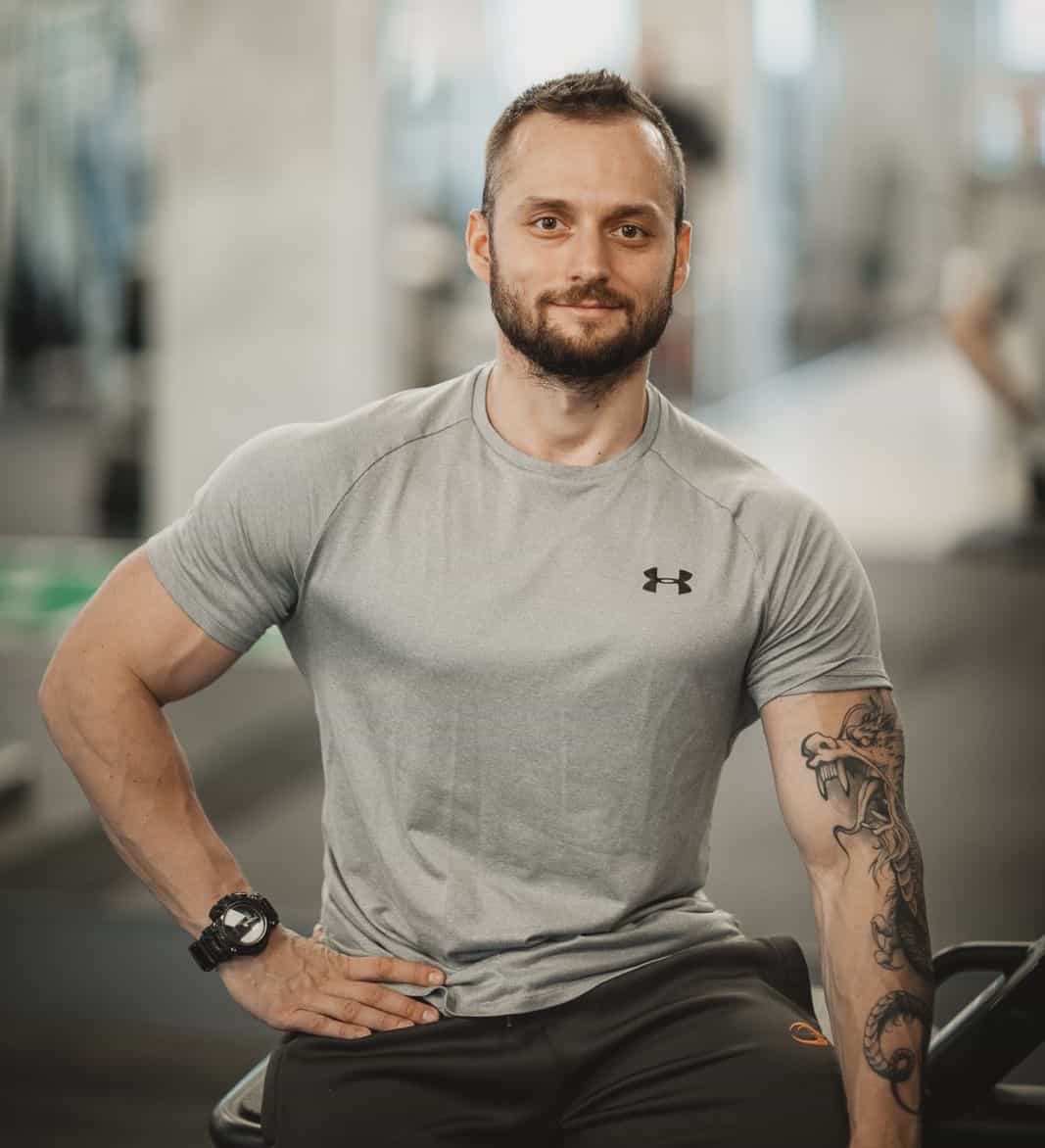 Trenér Jiří Kočvara sedící u zrcadla ve fitness centru TJ Lokomotiva Beroun, s rukama podél těla.